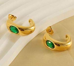 Close-up of gold C-shaped earrings featuring a faceted green gemstone on silk