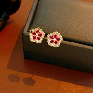 Close-up of flower stud earrings with red and white zircon in a grey jewelry box