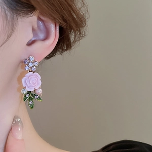 Detail view of pink rose and leaf earrings with pearl accents on a model's ear