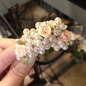 Close-up of elegant pearl hair tie featuring pink fabric roses and black elastic band