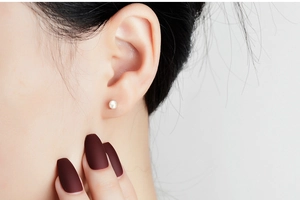 Close-up of 4-6mm white freshwater pearl stud earring worn on earlobe with soft luster