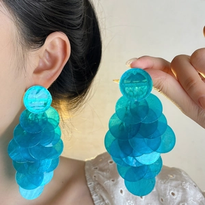 Detail showing oversized layered blue sequin tassel earrings worn for a visual size guide