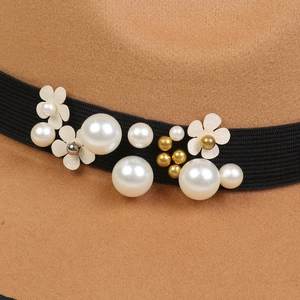 Detail of wool fedora featuring white pearls, beige flowers, and black grosgrain ribbon