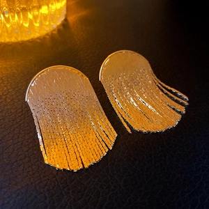 Elegant gold metallic curved tassel earrings with long bead chains on a black background