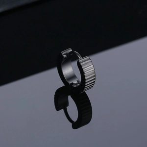 Macro shot of black titanium steel gear earring with striped texture on reflective background