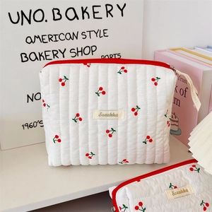 Detailed macro shot of white quilted cherry print cosmetic bag with red zipper closure