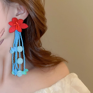 Detail of bohemian long beaded fringe earrings with red fabric flowers and blue beads