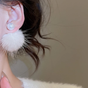Detail of white pompom and pearl stud earring shown worn for autumn elegance