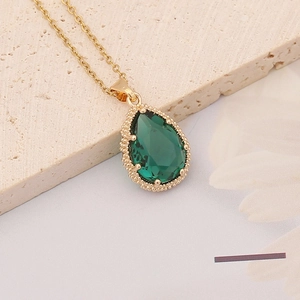 Macro detail of teardrop emerald zircon pendant with gold beaded edging and chain