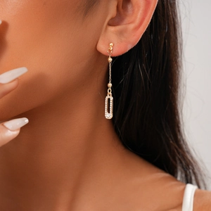 Close-up of a long golden drop earring with a rectangular rhinestone pendant