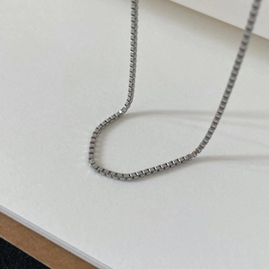 Detailed view of silver stainless steel box chain necklace on a minimalist white surface