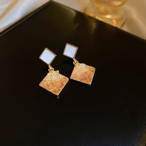 Detailed close-up of geometric gold earrings with amber crystals on a black display surface