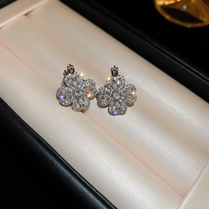 Elegant silver four-leaf clover earrings with zircon pavé setting on luxury silk background
