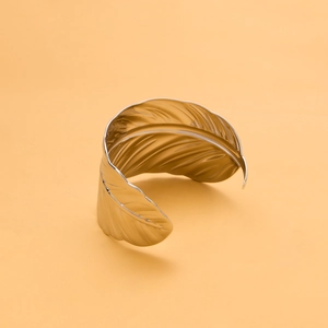 Detail of a vintage golden feather-shaped open bangle with intricate metallic texture