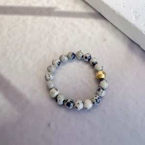 Minimalist Dalmatian Jasper beaded ring with a gold accent bead on a textured surface