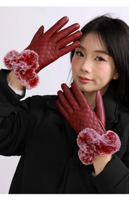 Close-up of red leather gloves featuring quilted diamond pattern and plush fur balls