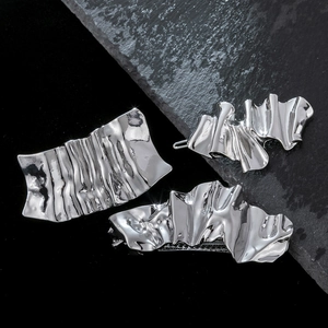 Detailed view of silver hair clips with irregular pleated texture on stone background