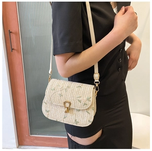 Detail of a beige woven straw bag featuring elegant green floral embroidery and gold metal clasp