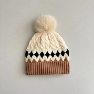 Close-up of cable knit pom pom beanie with geometric pattern and soft ribbed cuff