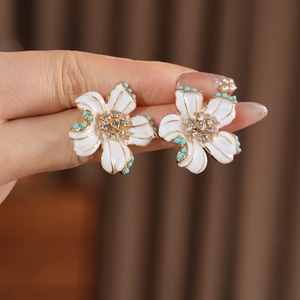 Gros plan sur des boucles d'oreilles fleur en émail blanc avec détails dorés et turquoise