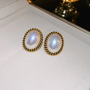 Gros plan sur boucles d'oreilles rétro en métal doré et pierre blanche ovale