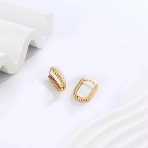 Macro view of gold-plated stainless steel U-shaped earrings with fine textured wave patterns