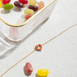 Close-up of golden chain bracelet featuring a red enamel heart pendant on marble surface