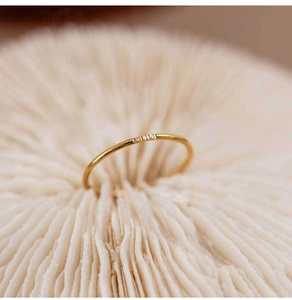 Detail of a slim gold band ring featuring three tiny zircons set in white coral stone