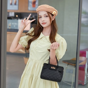 Chic black quilted handbag with gold buckle held by a model in a yellow dress