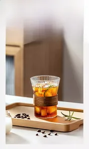 Close-up of vertical ribbed glass cup with wooden heat insulation sleeve and ice tea