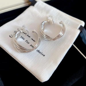Macro detail of silver twisted multi-layer hoop earrings on a white branded fabric pouch