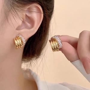 Detail view of multi-layer gold earrings with white zircon stones held in hand