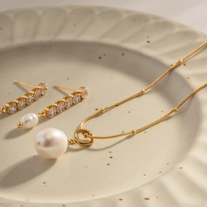Elegant gold titanium necklace with large pearl pendant and matching drop earrings on tray