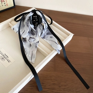 Detail showing elegant black bow hair claw clip with ink floral silk streamers on tray