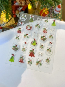 Macro shot of 3D Christmas nail art stickers featuring festive bells and wreaths