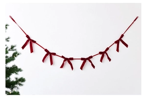 Detail of red velvet bow garland hanging on a wall next to a decorated Christmas tree
