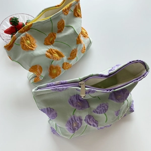 Détail de pochettes à cosmétiques en coton brodé avec motifs floraux orange et violets