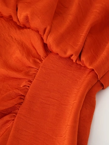 Close-up of vibrant orange pleated satin fabric showing rich texture and glossy finish