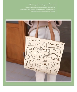 Detail of beige canvas tote bag with cartoon cat illustration and artistic text graphics