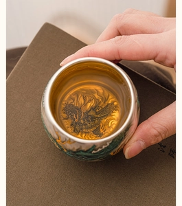 Close-up of silver-plated tea cup with golden interior and intricate dragon motif