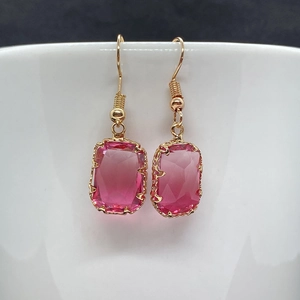 Dettaglio degli orecchini a gancio dorati con pendenti in cristallo rosa rettangolare