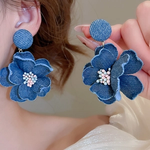 Macro shot of dark denim fabric flower earrings with textured frayed edges and beaded center