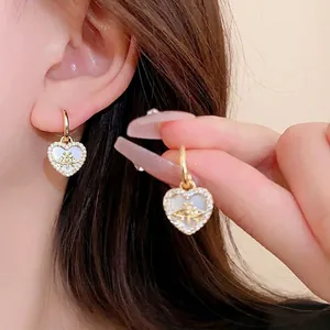 Détail d'une boucle d'oreille cœur dorée avec relief d'abeille sur nacre blanche