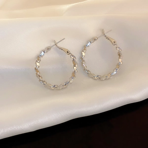 Minimalist silver-tone textured hoop earrings on premium white silk fabric background