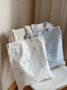 Detail of canvas tote bags featuring blue bow embroidery and striped cotton fabric