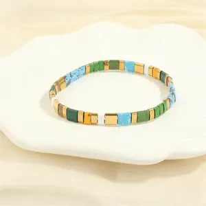 Detail of colorful Tila tile bead bracelet with gold accents on a white shell plate