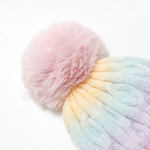 Close-up of rainbow cable knit texture and soft pink faux fur pompom on winter beanie