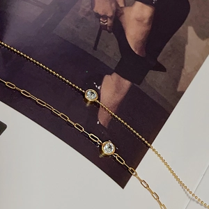 Close-up of golden paperclip chain and bead chain bracelet with round zircon stone inlay