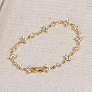 Detailed macro of gold clover bracelet with zircon flower links on white fabric