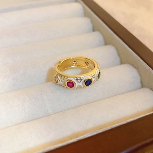Macro detail of gold ring with colorful gemstones and white heart patterns on velvet